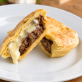 Illustrative square photo of a golden flaky savoury pie cut open to show mince and melted cheese